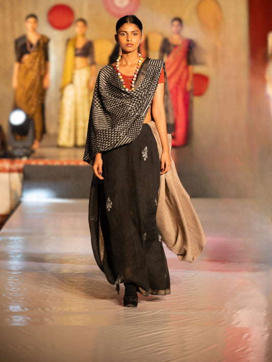 Model walking on a fashion show runway wearing a black and white patterned top with a long black skirt. Bani Thani Chandrika Saree by Soulweaves
