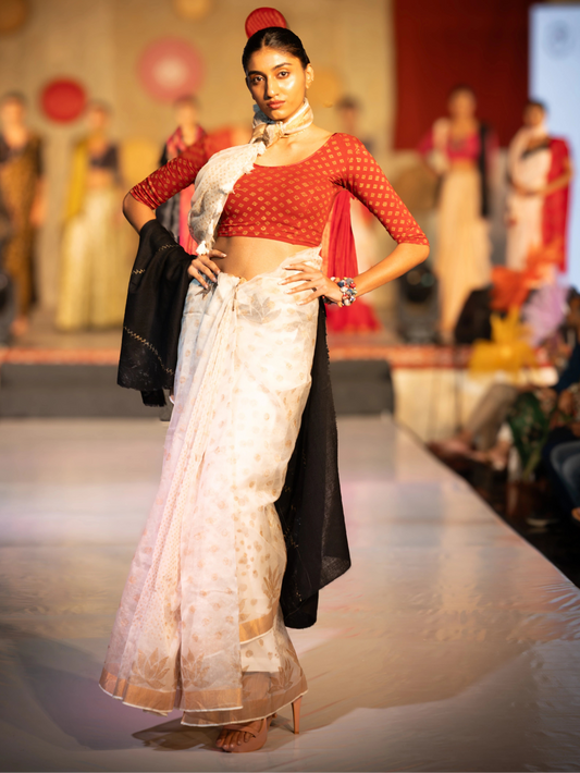Model walking on a fashion show runway wearing a red top and white saree. Bani Thani Kamalika Saree by Soulweaves