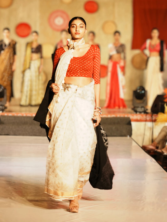 Model walking on a fashion show runway wearing a red top and white saree. Bani Thani Kamalika Saree by Soulweaves