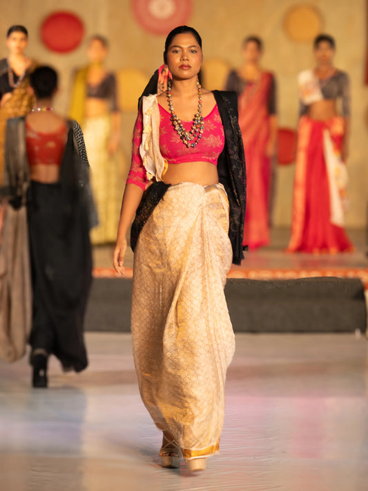 Model walking on a runway wearing a pink blouse and beige saree with other models in the background. Bani Thani Mridula Saree by Soulweaves