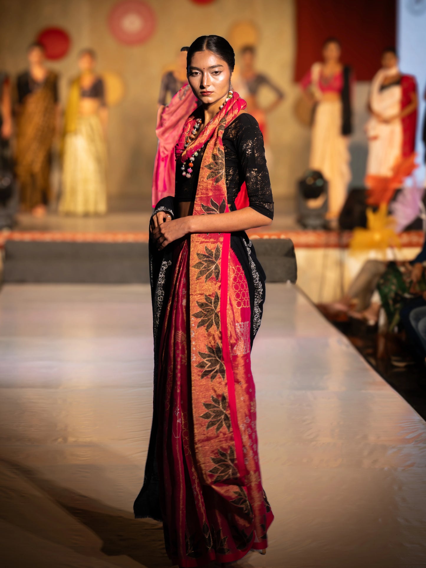 Model wearing a traditional outfit with a red and black saree on a fashion show runway. Bani Thani Padmapriya Saree by Soulweaves