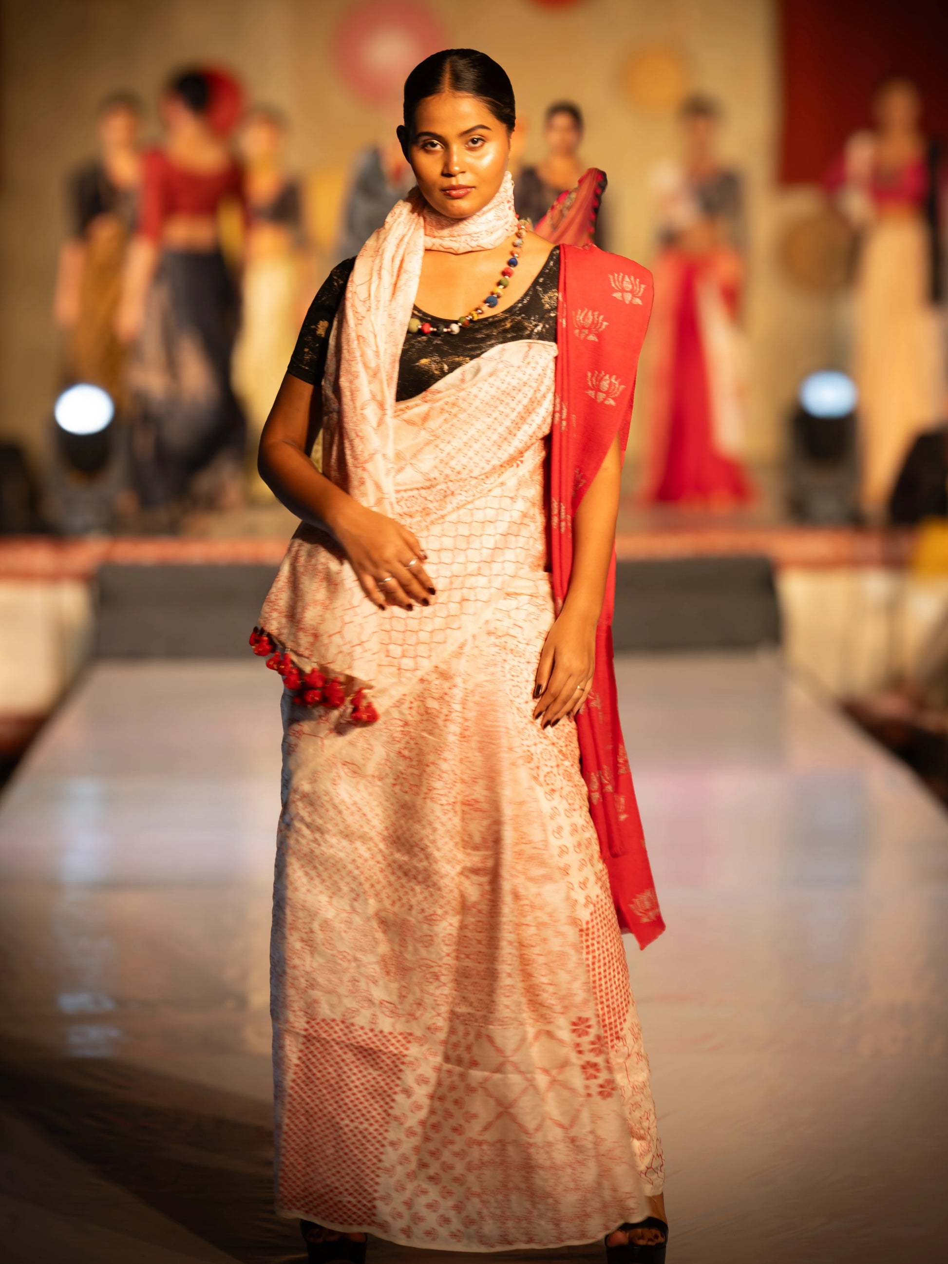 Model wearing a white saree with red border on a fashion show stage. Bani Thani Rudraja Saree by Soulweaves