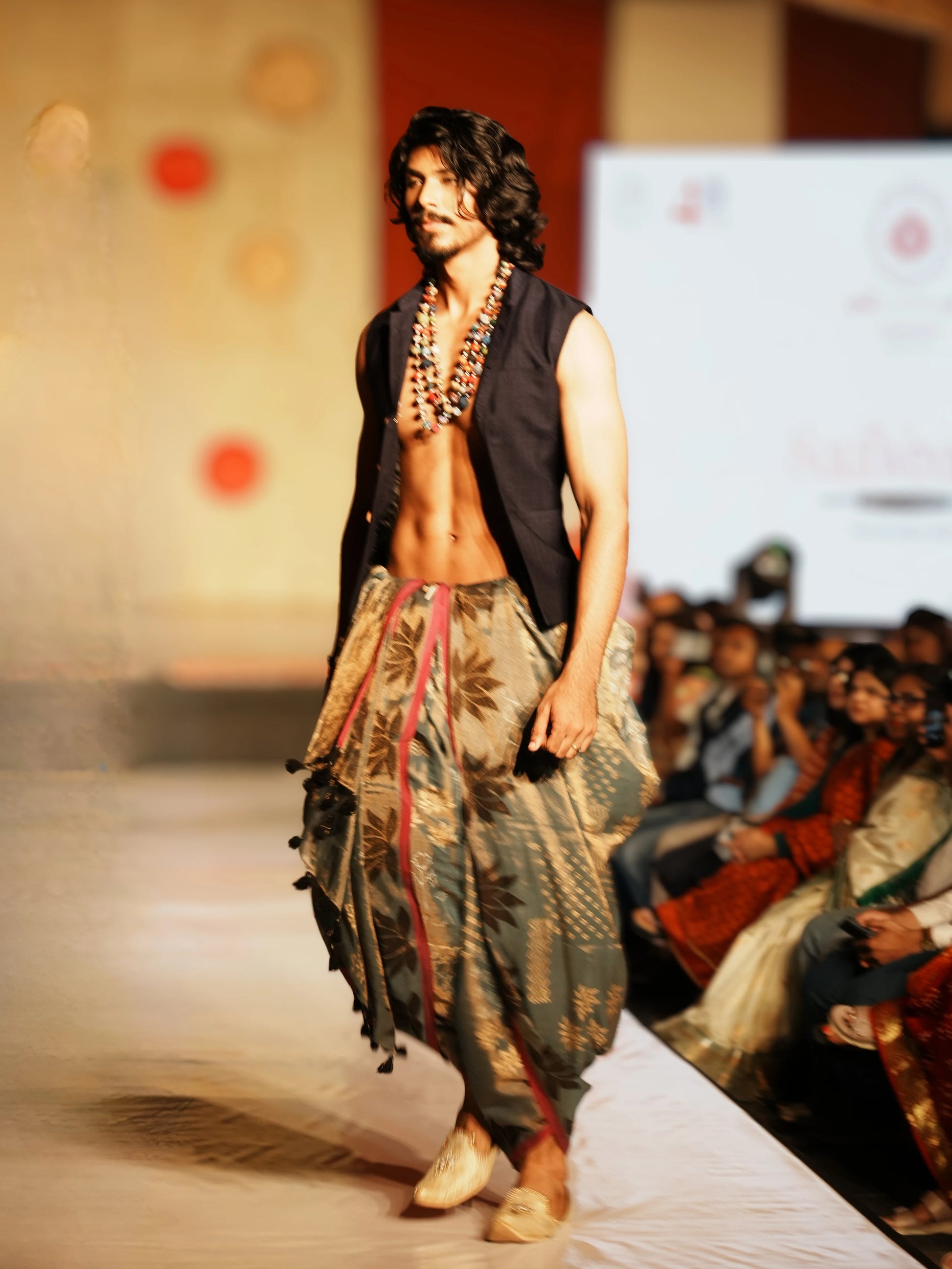 Man walking on a fashion show runway wearing a traditional outfit with a patterned dhoti and vest. Rudrangi Dhoti Saree by Soulweaves
