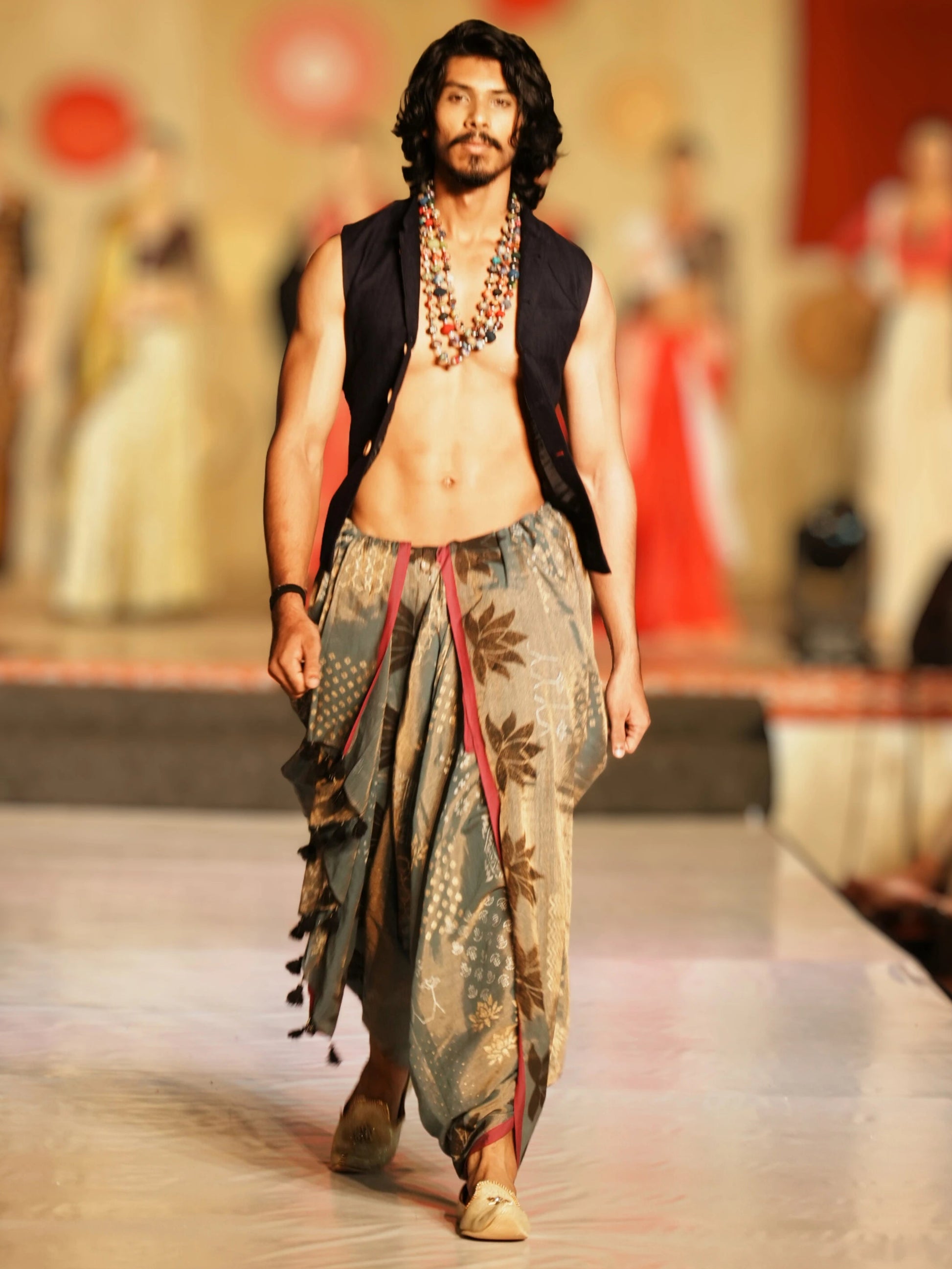 Man walking on a fashion show runway wearing a traditional outfit with a patterned dhoti and vest. Rudrangi Dhoti Saree by Soulweaves